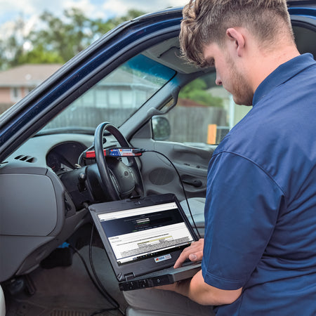 A mechanic using a Durabook S14i laptop inside a car for diagnostic purposes.