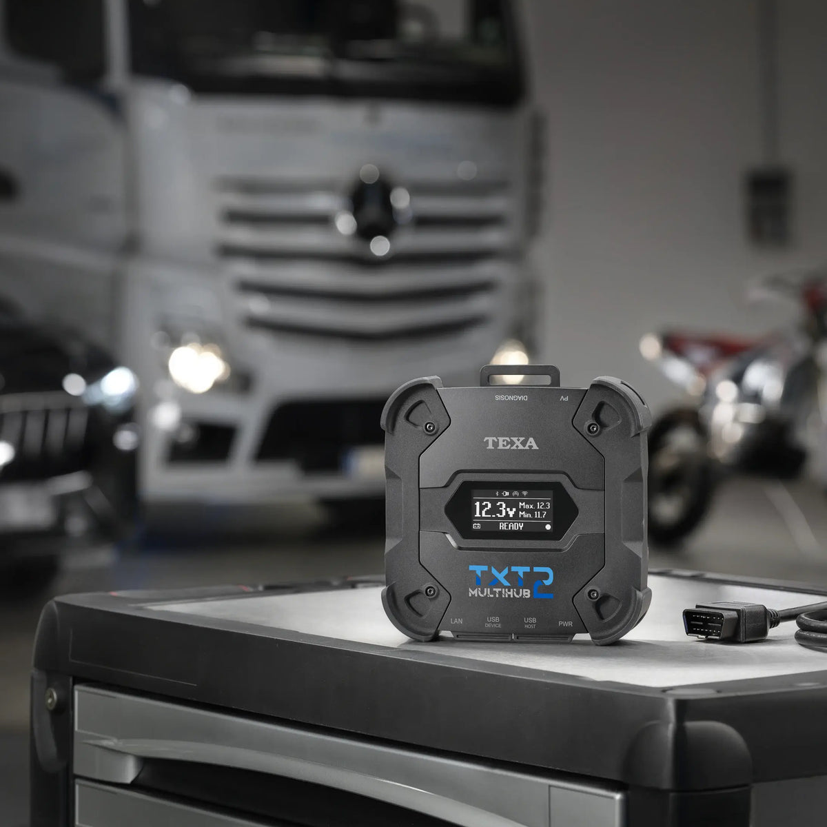 TEXA TXT2 with OBD cable on a toolbox with a Mercedes truck in the background blurred.