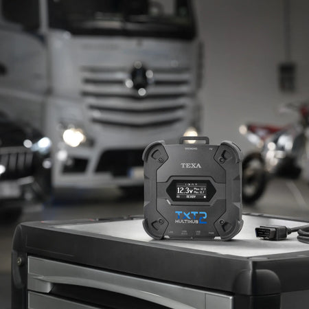TEXA TXT2 with OBD cable on a toolbox with a Mercedes truck in the background blurred.
